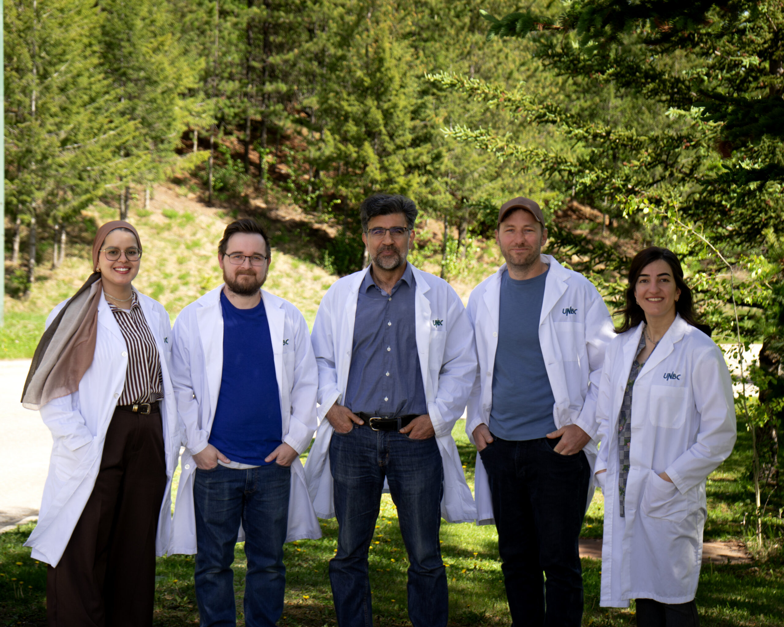 Five NALS team members wearing lab coats outdoors among trees.